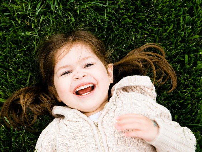 Happy young girl smiling at camera and laying on the grass