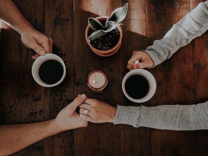 Two people hold hands over a table while drinking coffee